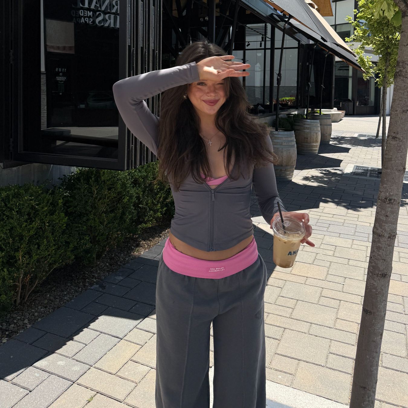 The coach smiles and shields her eyes from the sun on a sunny street.
